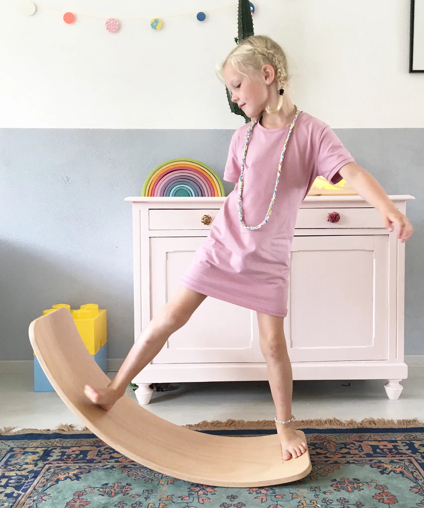 Wobbel original balance board, made from beech wood, being played with by young girl in a playroom.