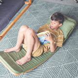 Wobbel XL wooden balance board toy for older kids or adults with padded cushion deck and matching pillow in green, with child laying and reading on it.