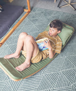 Wobbel XL wooden balance board toy for older kids or adults with padded cushion deck and matching pillow in green, with child laying and reading on it.