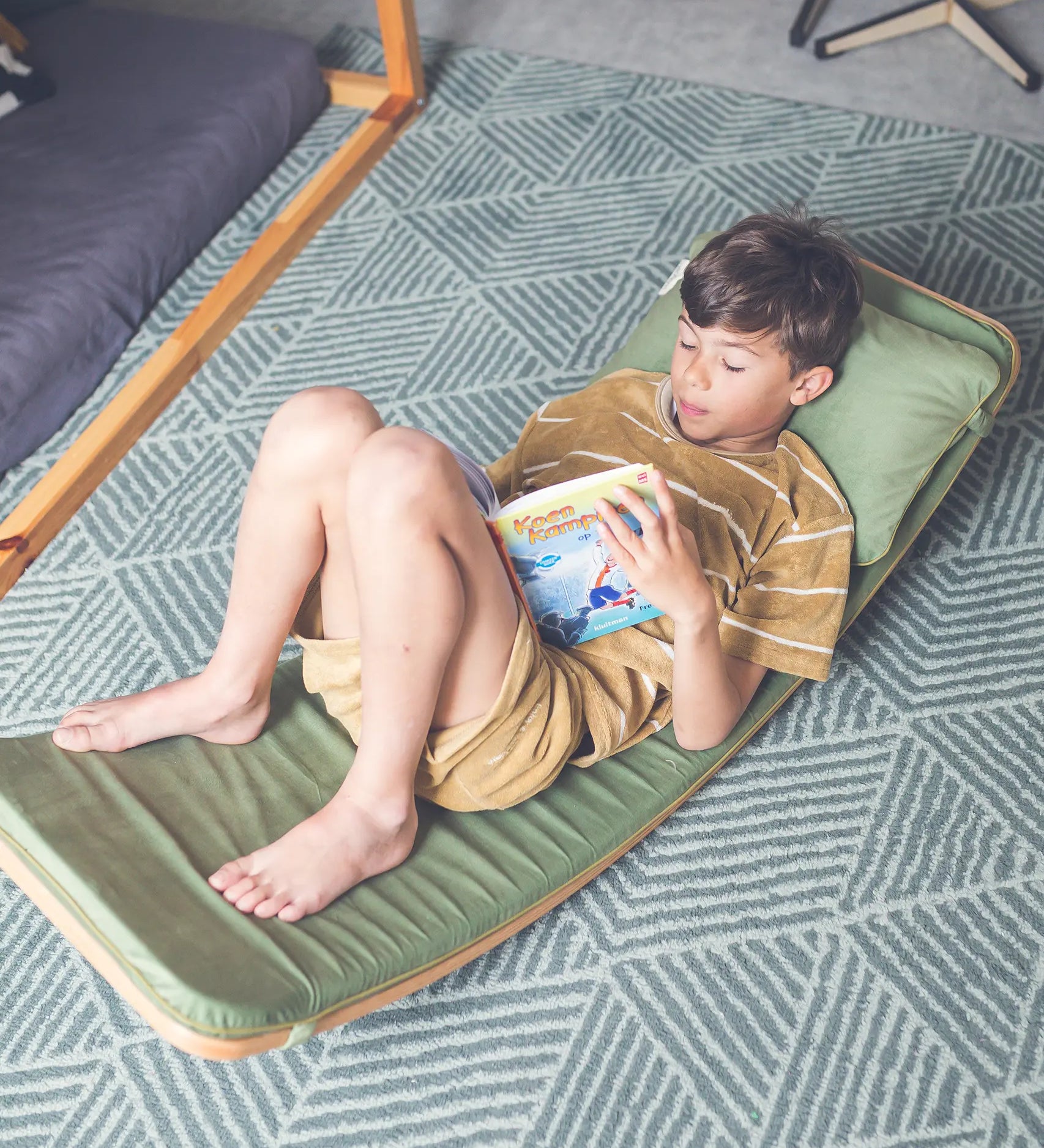 Wobbel XL wooden balance board toy for older kids or adults with padded cushion deck and matching pillow in green, with child laying and reading on it.