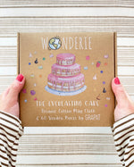 Wonderie cake play cloth box in hands. A three tier birthday play cloth with 60 Grapat wooden play food decoration pieces and paper invitations.