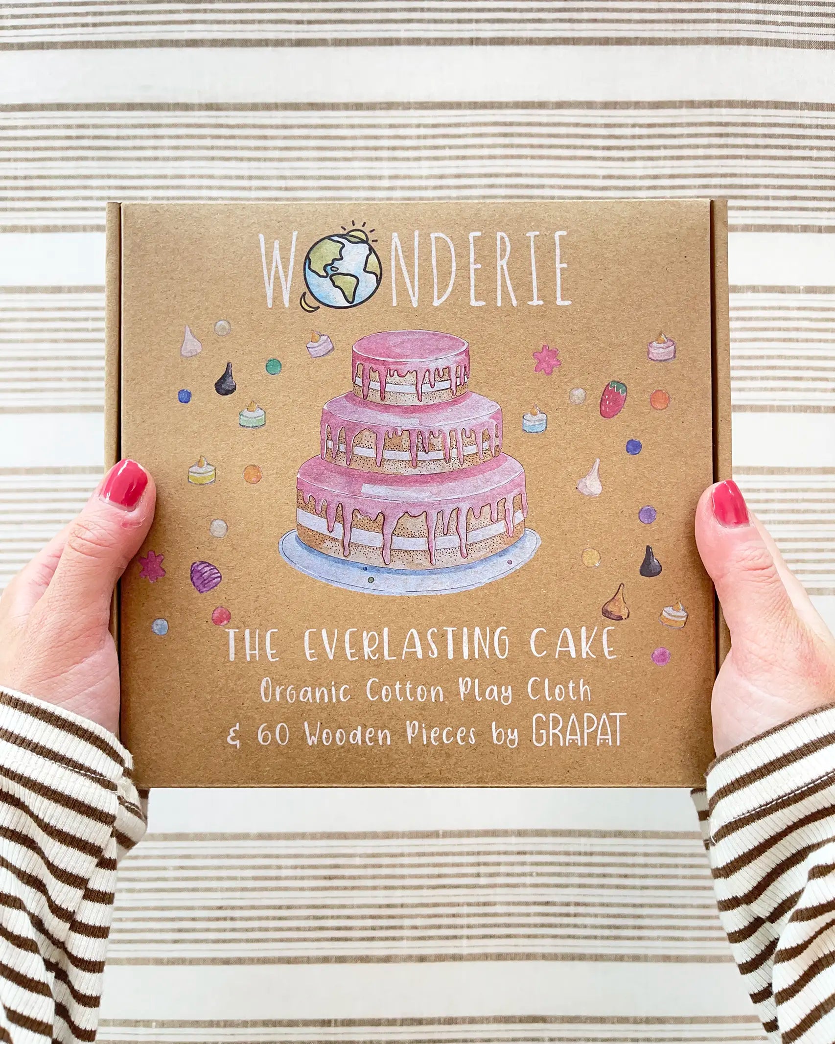 Wonderie cake play cloth box in hands. A three tier birthday play cloth with 60 Grapat wooden play food decoration pieces and paper invitations.