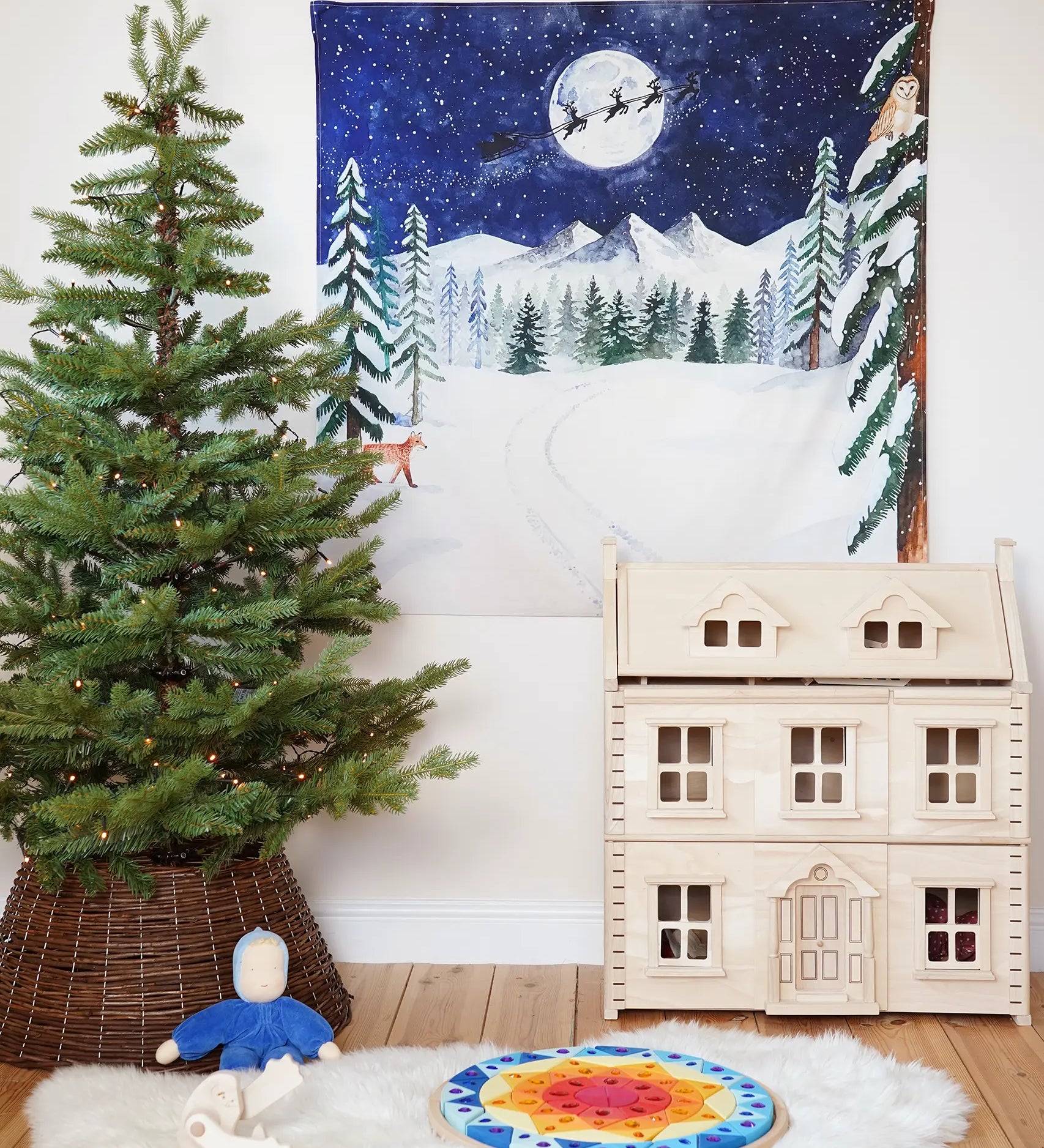 Wonderie Christmas Cotton Play Cloth, One Starry Winter's Night, a snowy forest scene with Santa and his sleigh in the Babipur playroom next to a PlanToys Victorian Dollhouse and Christmas tree.