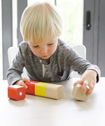 A child sat at a white table, playing with the Tegu Magnetic Wooden Blocks 