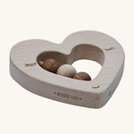 A side view of the Wooden Story Heart Rattle, showing the natural wood grain of the rattle, and the words "Wooden Story" etched onto the side of the rattle.