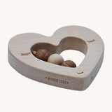 A side view of the Wooden Story Heart Rattle, showing the natural wood grain of the rattle, and the words "Wooden Story" etched onto the side of the rattle.