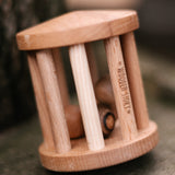 The Wooden Story Turtle Dove Rattle on its side, to show it can be twirled like a spinning top. The natural wood grain of the rattle and wooden balls shows through, and the words "Wooden Story" is etched onto the side of the rattle.
