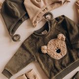 A flatlay showing the Wooly Organic embroidered sweater in tea leaf /savannah available at Babipur with the tea leaf and pale blush hat with teddy bear ears 