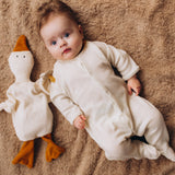 A baby lying on it's back next to a Wooly Organic goose heating pad available at Babipur. This heating pad has a pacifier tied on the arm
