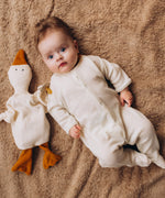 A baby lying on it's back next to a Wooly Organic goose heating pad available at Babipur. This heating pad has a pacifier tied on the arm