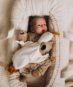 A baby lying in a basket and holding the Wooly Organic goose heating pad available at Babipur with a pacifier tied on the arm