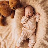 A top down image of a baby lying on their back next to the Wooly Organic soft teddy bear in caramel brown available at Babipur.