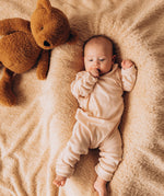 A top down image of a baby lying on their back next to the Wooly Organic soft teddy bear in caramel brown available at Babipur.