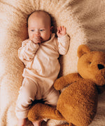A close up of a baby lying on a soft and cuddly blanket next to the Wooly Organic soft teddy bear in caramel brown available at Babipur