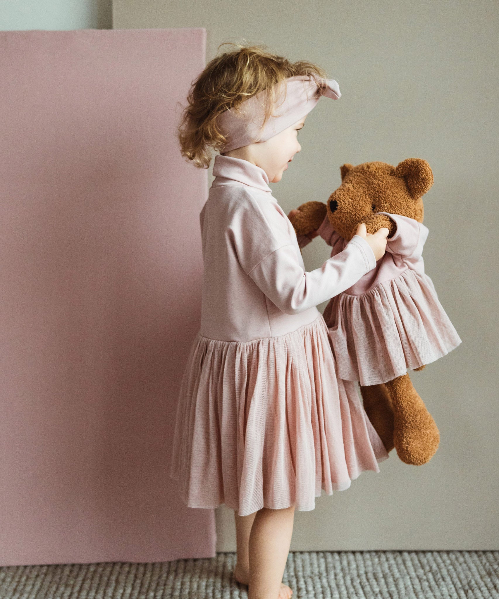 A child playing with the Wooly Organic soft teddy bear in caramel brown with a pink tutu available at Babipur.