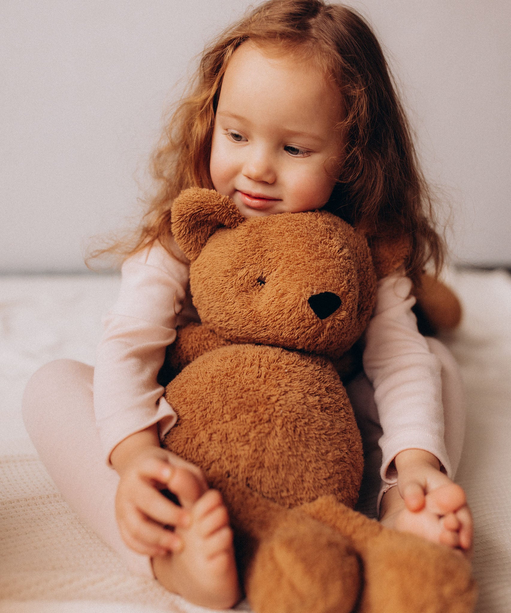 A close up of a small child holding the Wooly Organic soft teddy bear in caramel brown showing the cute facial features. Teddy bear  available at Babipur.
