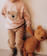 A close up of a child holding the Wooly Organic soft teddy bear in caramel brown by the hand. Teddy bear available at Babipur.