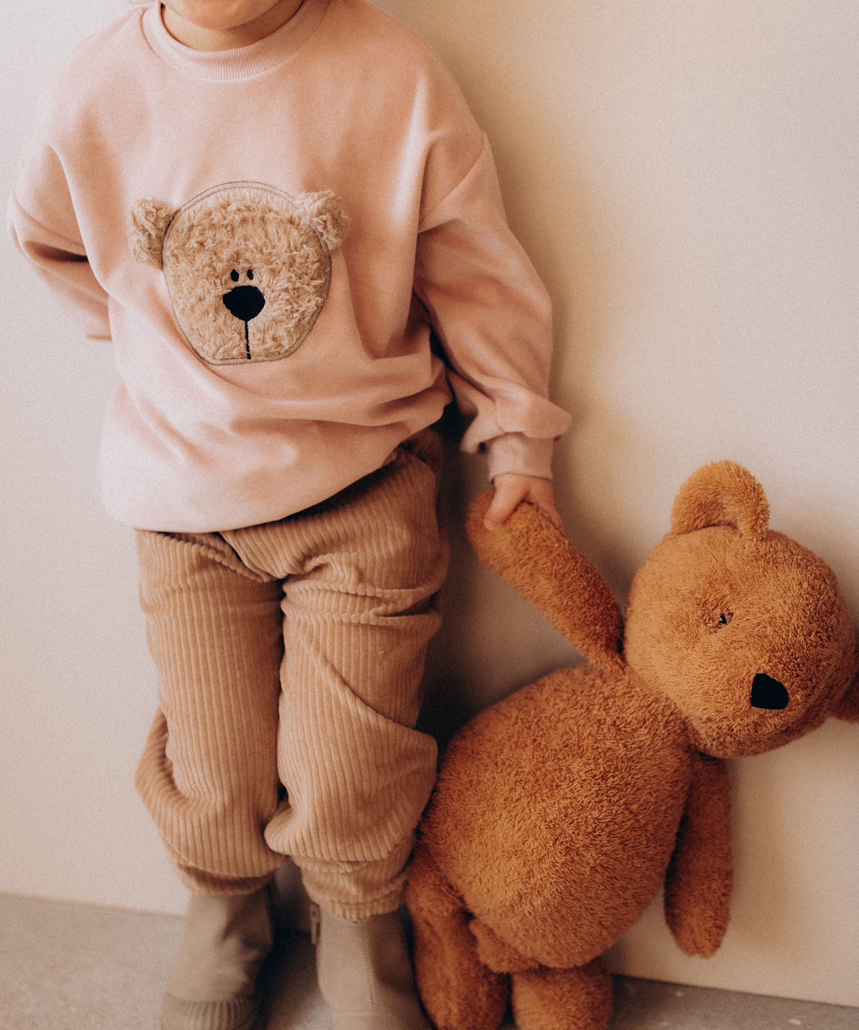A close up of a child holding the Wooly Organic soft teddy bear in caramel brown by the hand. Teddy bear available at Babipur.