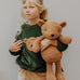 Child holding a large Wooly Organic teddy bear toy, made from organic cotton, in a caramel brown, for sale at Babipur.
