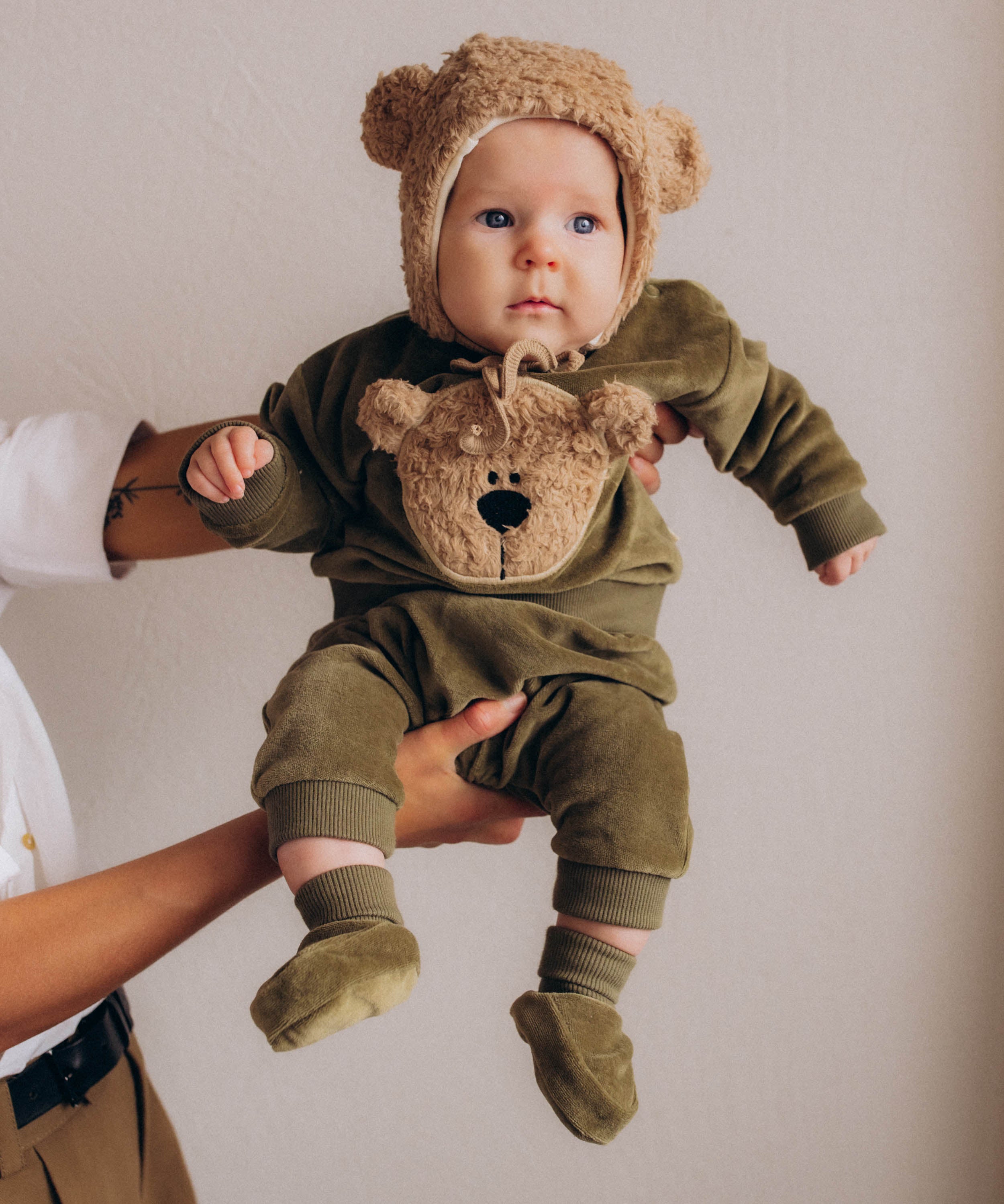 A baby wearing the Wooly Organic embroidered sweater in tea leaf /savannah available at Babipur showing the popper fastener detail
