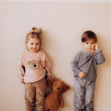 A child holding the Wooly Organic soft teddy bear by the hand and wearing the velour hair scrunchy, both available at Babipur.