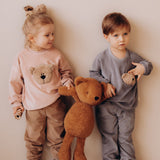 2 small children holding the Wooly Organic soft teddy bear in caramel brown by the hand. Teddy bear available at Babipur.