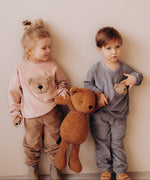 2 small children holding the Wooly Organic soft teddy bear in caramel brown by the hand. Teddy bear available at Babipur.