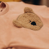 A stack of the Wooly Organic embroidered teddy bear velour sweater in pale blush pink /savannah available at Babipur. 