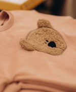 A stack of the Wooly Organic embroidered teddy bear velour sweater in pale blush pink /savannah available at Babipur. 
