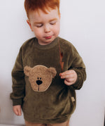 A child modelling the the Wooly Organic embroidered GOTS organic cotton velour sweater in tea leaf /savannah available at Babipur showing the fluffy teddy embroidery on the front