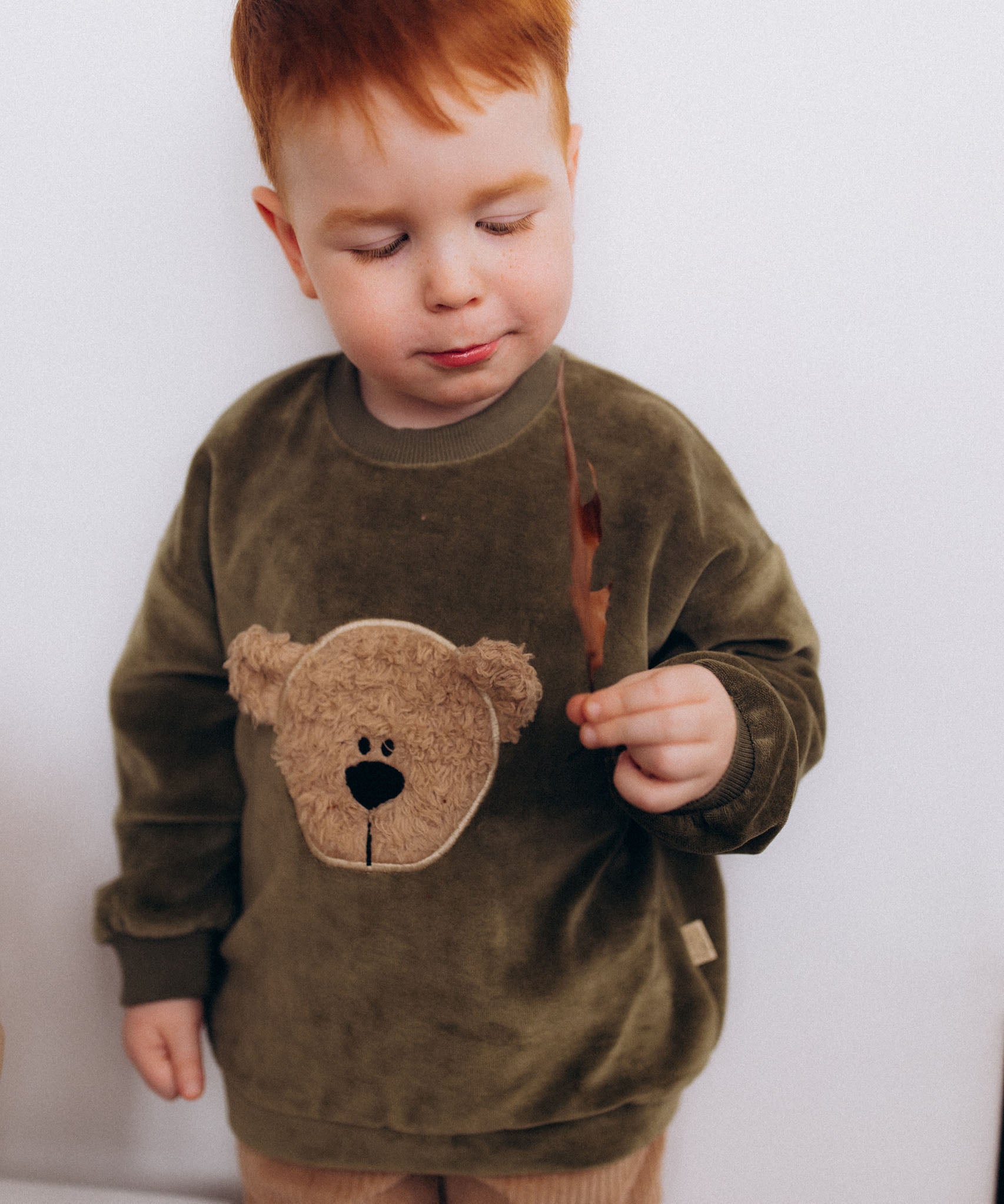 A child modelling the the Wooly Organic embroidered GOTS organic cotton velour sweater in tea leaf /savannah available at Babipur showing the fluffy teddy embroidery on the front