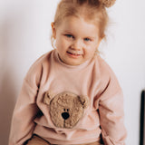 A close up of a child wearing the Wooly Organic embroidered velour sweater in pale blush pink /savannah available at Babipur showing the cute fluffy teddy bear detail 