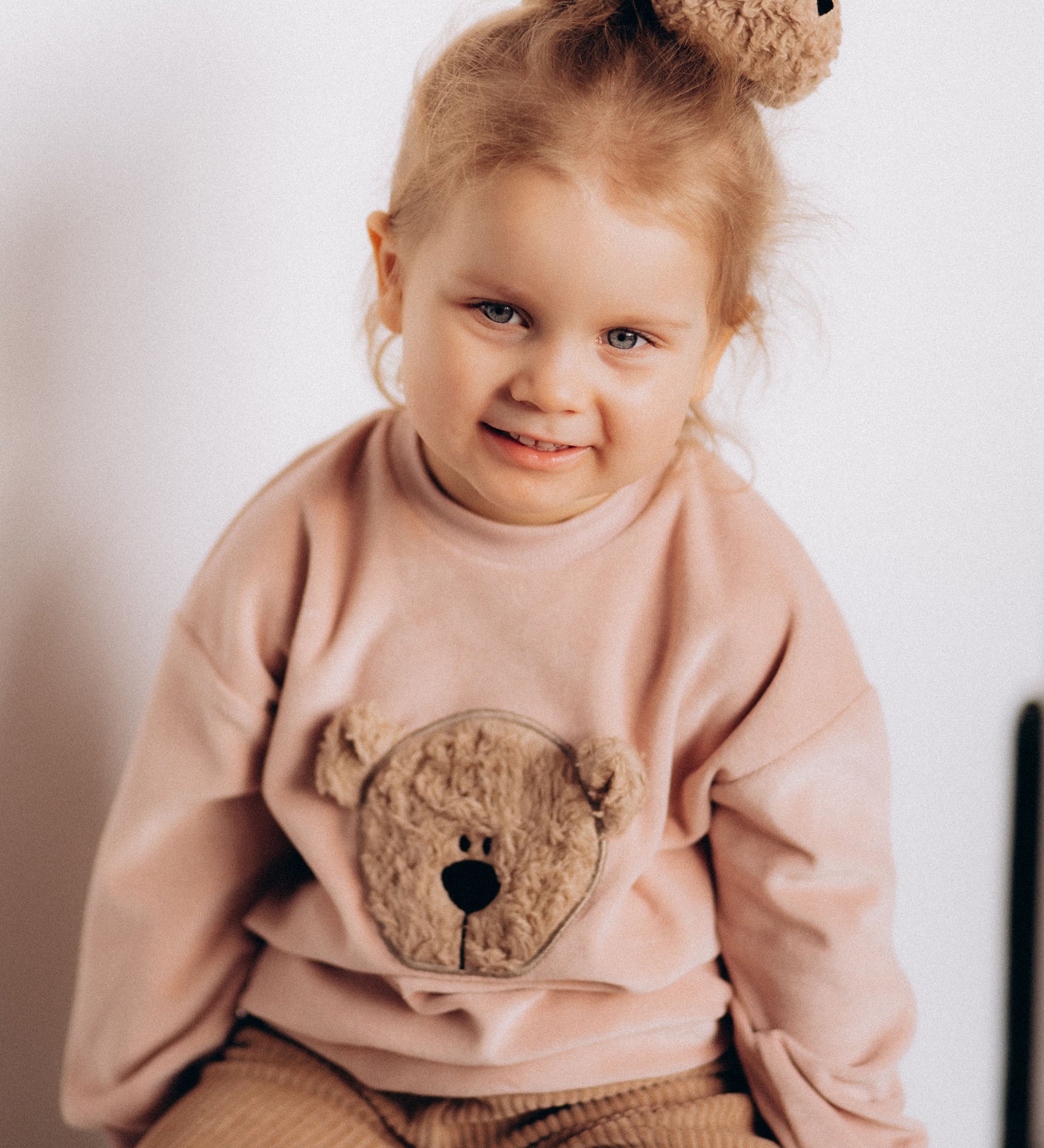 A close up of a child wearing the Wooly Organic embroidered velour sweater in pale blush pink /savannah available at Babipur showing the cute fluffy teddy bear detail 