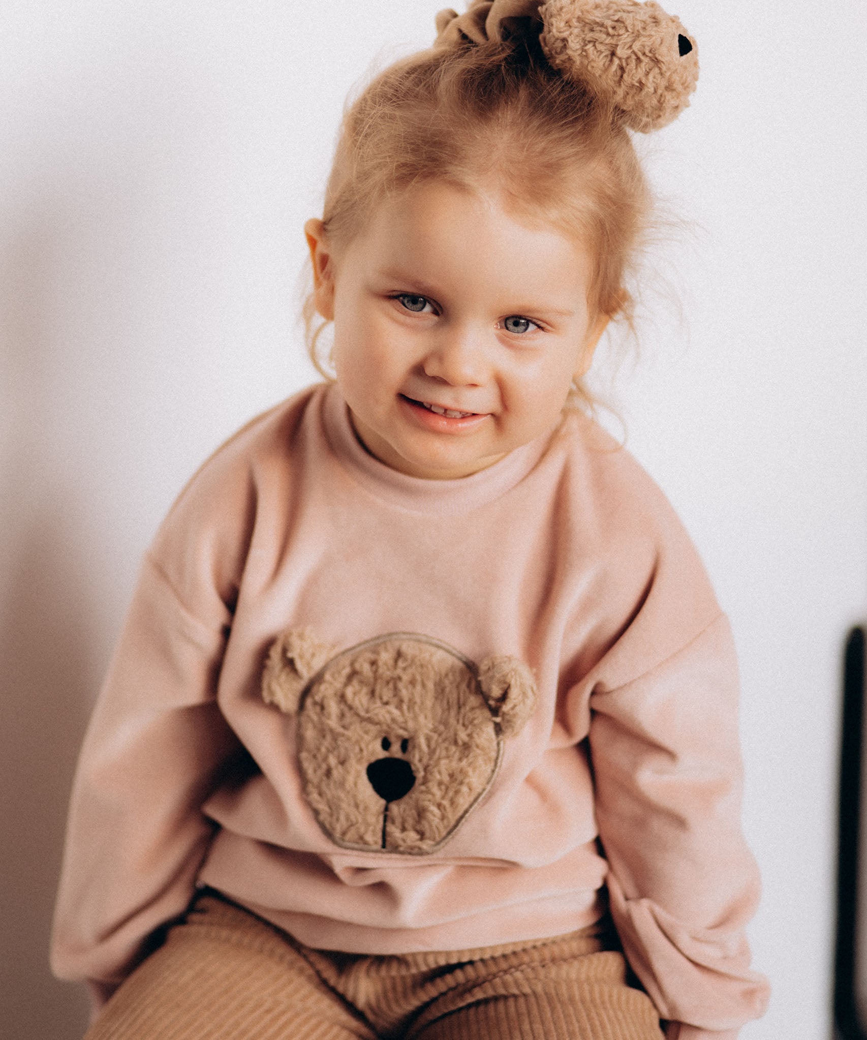 A close up of a child wearing the Wooly Organic embroidered velour sweater in pale blush pink /savannah available at Babipur showing the cute fluffy teddy bear detail 