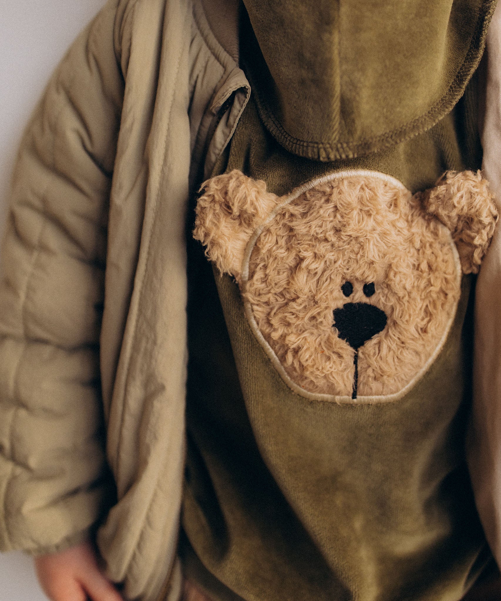 A close up of the cute fluffy cream teddy embroidery on the Wooly Organic  velour sweater in tea leaf /savannah available at Babipur. 