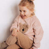 A child sitting down and wearing the Wooly Organic embroidered velour sweater in pale blush pink /savannah and matching scrunchy both available at Babipur 