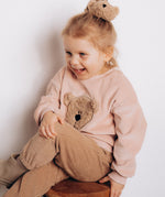 A child sitting down and wearing the Wooly Organic embroidered velour sweater in pale blush pink /savannah and matching scrunchy both available at Babipur 