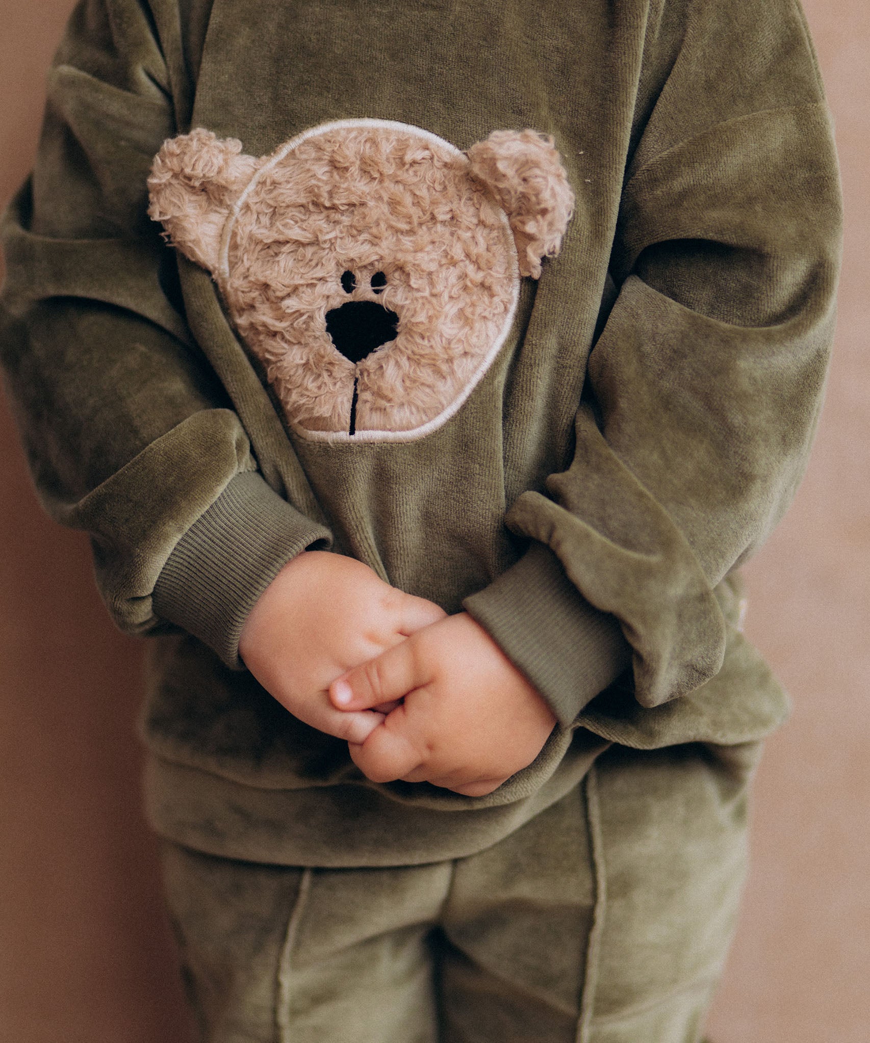 A close up of the velour detail and cute fluffy cream teddy embroidery on the A child wearing the Wooly Organic GOTS organic cotton velour sweater in tea leaf /savannah available at Babipur. 