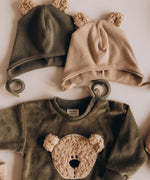 A flatlay showing the Wooly Organic hat with teddy bear ears in tea leaf /savannah next to the velour sweater, both  available at Babipur 