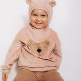 A child sitting down and wearing the Wooly Organic GOTS organic cotton embroidered velour sweater in pale blush pink /savannah available at Babipur