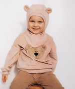 A child sitting down and wearing the Wooly Organic GOTS organic cotton embroidered velour sweater in pale blush pink /savannah available at Babipur