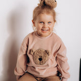 A child sitting down and wearing the Wooly Organic embroidered velour sweater in pale blush pink /savannah available at Babipur. 