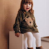 A child sitting on a wooden box and wearing the Wooly Organic embroidered GOTS organic cotton velour sweater in tea leaf /savannah available at Babipur. 