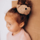 A close up of the cute fluffy teddy bear attached to the Wooly Organic scrunchy worn by a child and available at Babipur.