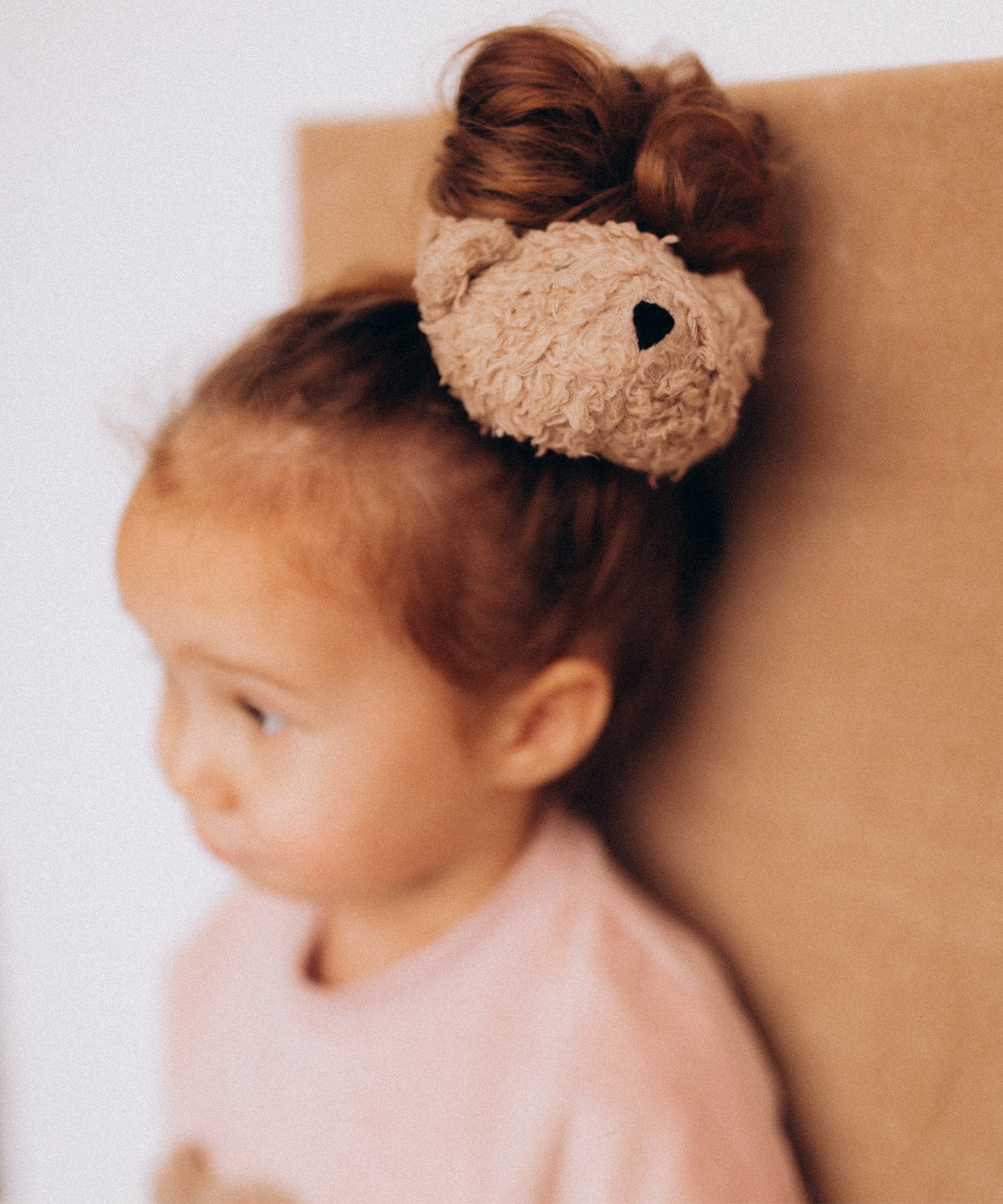 A close up of the cute fluffy teddy bear attached to the Wooly Organic scrunchy worn by a child and available at Babipur.