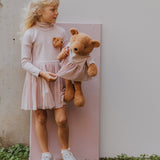 A older child holding the Wooly Organic soft teddy bear in caramel brown with a pink tutu available at Babipur. 