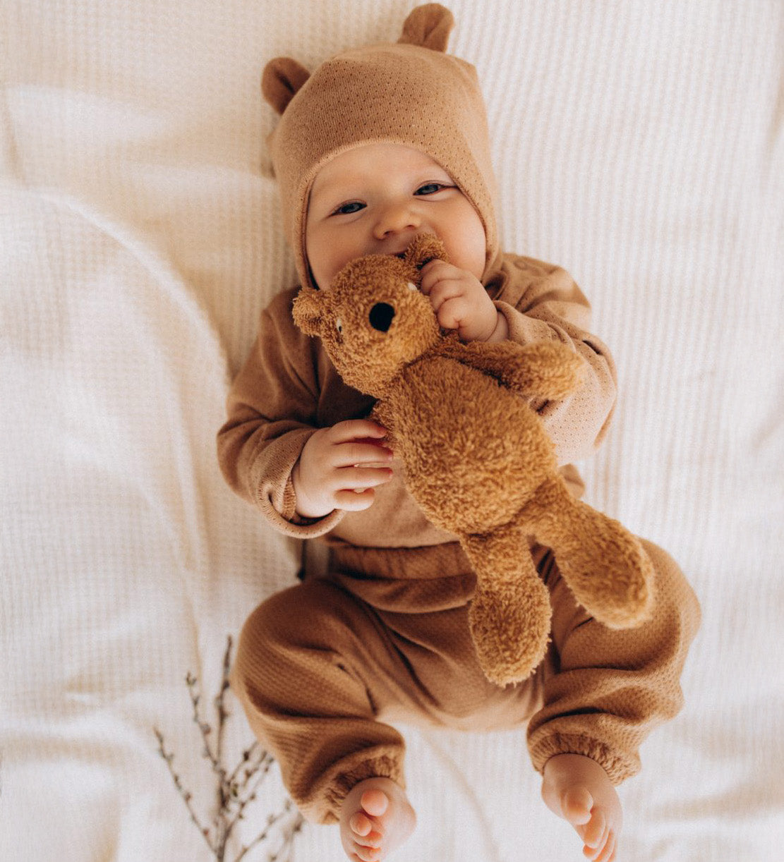 A baby holding and playing with the A small Wooly Organic soft teddy bear in brown available at Babipur. 