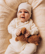 A baby lying on a wooly blanket and holding onto a small Wooly Organic soft teddy bear in brown available at Babipur. 