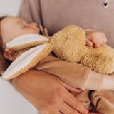 A sleeping baby holding a small Wooly Organic soft bunny rabbit toy in light brown available at Babipur. 