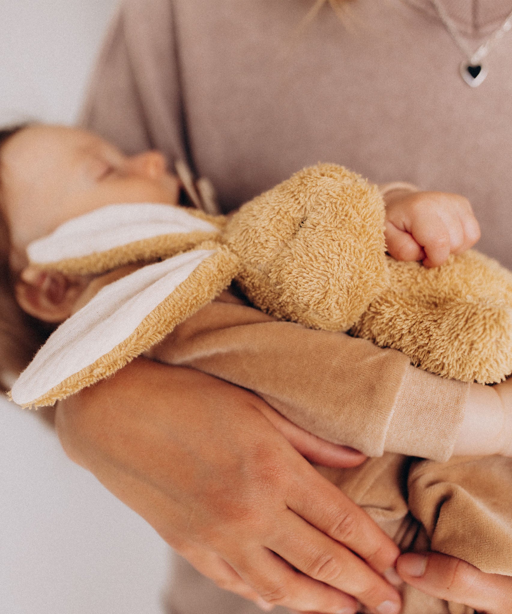 A sleeping baby holding a small Wooly Organic soft bunny rabbit toy in light brown available at Babipur. 